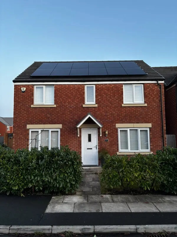 Black solar panels across the roof of a detached red-brick house