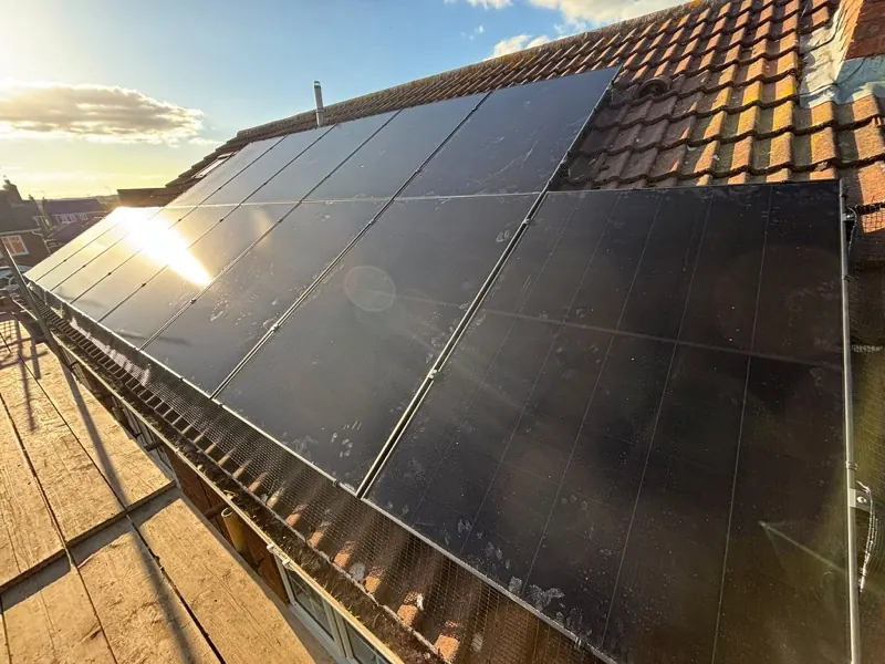 Black solar panels on a tiled roof with the sun behind